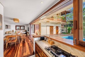 A modern kitchen with a large island, wooden flooring, and a view of a swimming pool. - Deluxe King Suite at Villa Lux Do Mar (Jijoca de Jericoacoara)