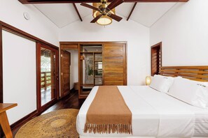 A bedroom with a bed, wooden headboard, a ceiling fan, and a view of a garden through a door.