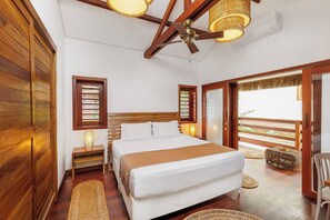 A bedroom with a wooden ceiling fan, a bed with white linens, a nightstand with a lamp, and a view of the outdoors through a sliding door. - Deluxe King Suite at Villa Lux Do Mar (Jijoca de Jericoacoara)
