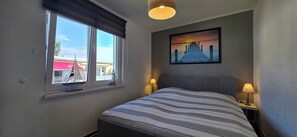 A bedroom with a bed, two bedside lamps, a window with a view, and a painting on the wall. - The Ultimate Vacation: Your Modern 4-Star Coastal Oasis Near the Forest in Graal-Müritz for ma (Graal-Müritz)
