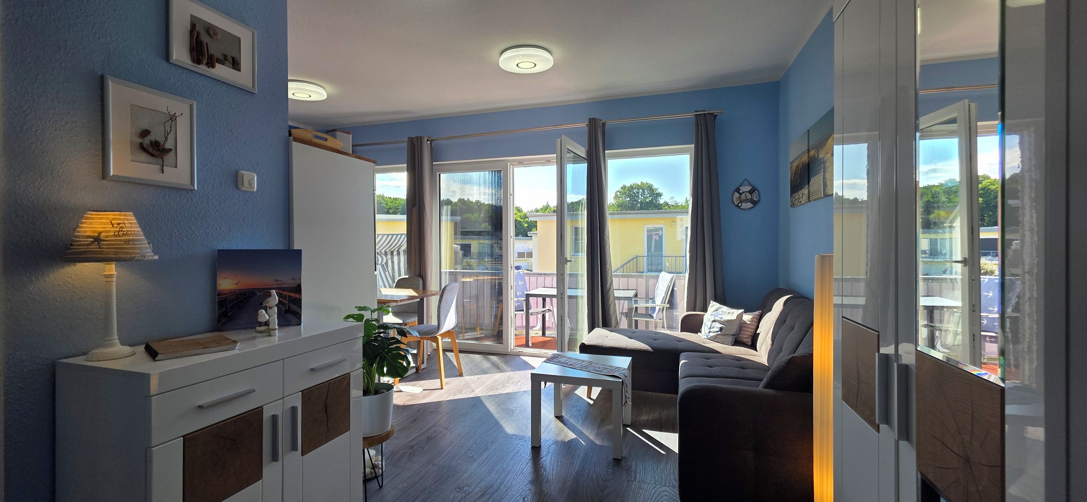 Un salon moderne comprenant un canapé, une table basse et un coin repas. Une grande fenêtre offre une vue sur l’extérieur.