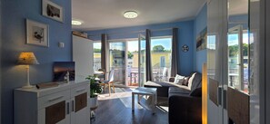 Un salon moderne comprenant un canapé, une table basse et un coin repas. Une grande fenêtre offre une vue sur l’extérieur.