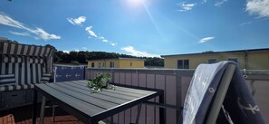 Eine Dachterrasse mit Tisch und Stühlen, einem Blumentopf und Blick auf die umliegenden Gebäude.