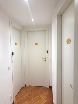 A hallway with two white doors, each with a gold plaque. The floor is wooden, and there is a light fixture on the ceiling. - 7 CENTRALE - Family Room (Milano)