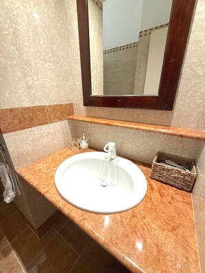 A bathroom with a marble sink, a mirror, and a wicker basket. - 7 CENTRALE - Family Room (Milano)