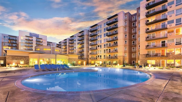 Ein Hotel mit Schwimmbad, mehreren Balkonen und einem Sonnenuntergangshimmel.
