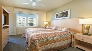 Ein Hotelzimmer mit Bett, Schreibtisch, Stuhl, Deckenventilator, Fenster mit Jalousien und einem Bild an der Wand.