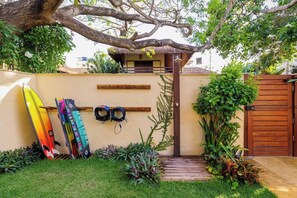A garden with a wooden fence, a thatched-roof structure, and two surfboards leaning against the wall.