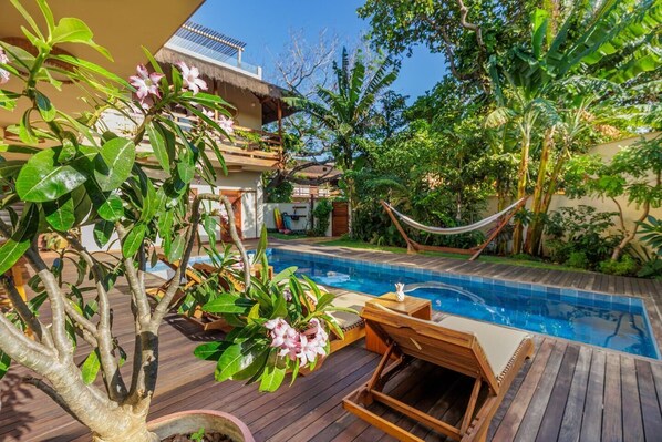 A pool area with wooden deck, lounge chairs, and a hammock.