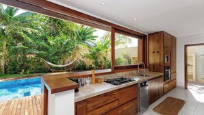 A modern kitchen with a large window, wooden cabinets, a gas stove, and a built-in dishwasher. - Honeymoon suite with a private rooftop Jacuzzi (Jijoca de Jericoacoara)