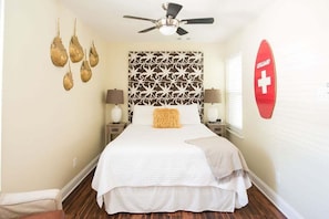 A bedroom with a bed, two bedside tables with lamps, a ceiling fan, a wall-mounted life guard sign, and a patterned headboard.