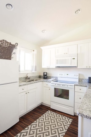 A kitchen with white cabinets, a microwave, a stove, and a coffee maker.