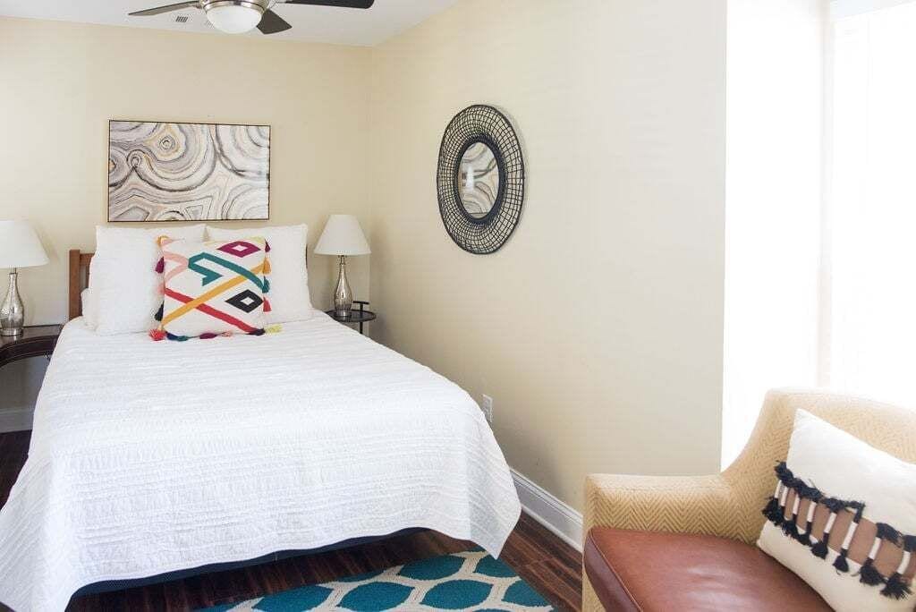 A hotel room with a bed, two bedside lamps, a wall-mounted mirror, and a decorative pillow.
