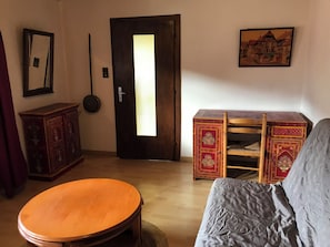 A room with a wooden door, a round table, a sofa, a cabinet, and a wall-mounted picture.
