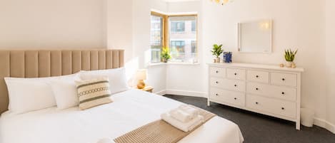 Et hotelværelse med en stor seng, et natbord, en kommode, et vindue med udsigt til bygninger og en unik loftlampe.