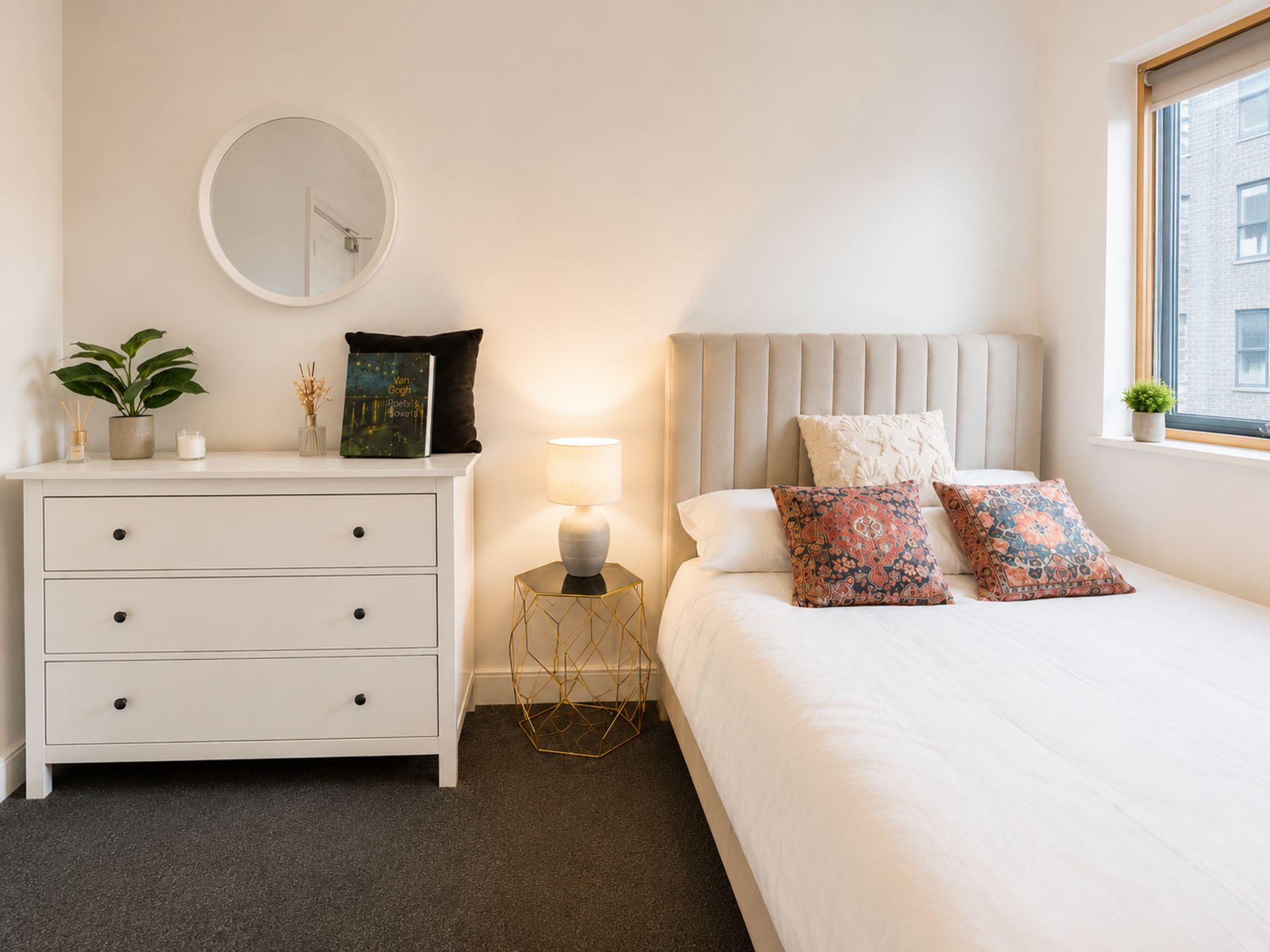 Un dormitorio con cama, mesitas de noche, lámpara, espejo y ventana.