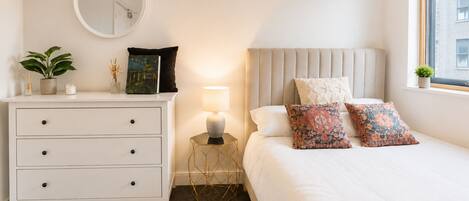 Un dormitorio con cama, mesitas de noche, lámpara, espejo y ventana.
