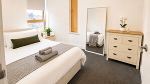 Ein Hotelzimmer mit Bett, Schminktisch, Spiegel und Fenster mit Blick auf Gebäude.
