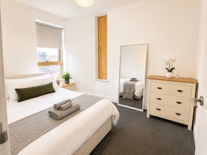 Ein Hotelzimmer mit Bett, Schminktisch, Spiegel und Fenster mit Blick auf Gebäude.