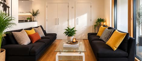 Uma sala de estar moderna com dois sofás pretos, uma mesa de centro de vidro e uma estante de livros.