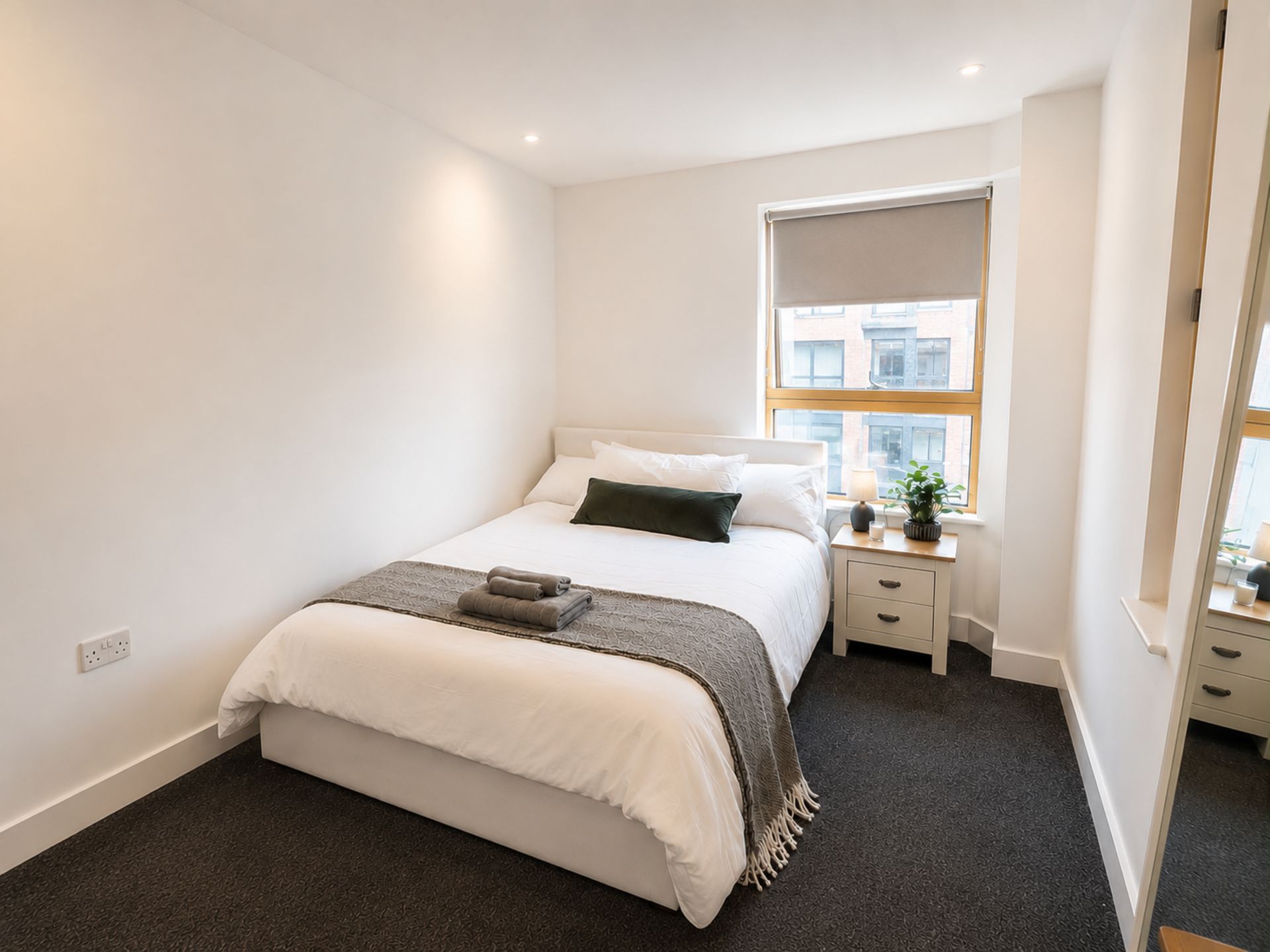 Quarto moderno com cama, mesas de cabeceira, uma janela e vista para edifícios.