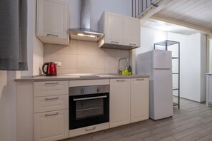 A modern kitchen with white cabinetry, a built-in oven, a stainless steel range hood, and a white refrigerator. - Caduti di Via Fani by Wonderful Italy (Bologna)