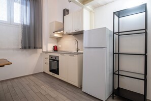 Une cuisine compacte avec des meubles blancs, un four encastré, un évier en acier inoxydable et un réfrigérateur blanc.