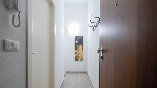A hallway with a wooden door, a light switch, a telephone, and a wall-mounted picture. - Caduti di Via Fani by Wonderful Italy (Bologna)