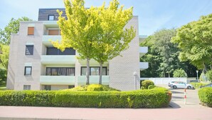 A modern multi-story residential building with balconies, a tree in the foreground, and a parking area with cars. - Sandkorn 6, cozy vacation rental in Grömitz with a terrace, garden, and 2 bedrooms (Grömitz)