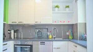 A modern kitchen with white cabinetry, a stainless steel dishwasher, a built-in oven, and a kitchen island with a sink. - Sandkorn 6, cozy vacation rental in Grömitz with a terrace, garden, and 2 bedrooms (Grömitz)