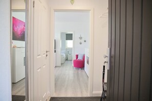 A hallway leading to a bedroom with a bed, a nightstand, and a red chair. - Sandkorn 6, cozy vacation rental in Grömitz with a terrace, garden, and 2 bedrooms (Grömitz)