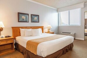 Ein Hotelzimmer mit einem großen Bett, zwei Nachttischen, einem Fenster mit Jalousien und zwei gerahmten Bildern an der Wand.