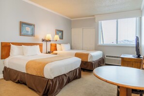 Ein Hotelzimmer mit zwei Betten, einem Schreibtisch, einem Stuhl, einem Fernseher und einem Fenster mit Jalousien.