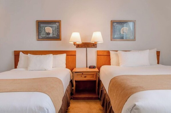 Ein Hotelzimmer mit zwei Einzelbetten, einem Nachttisch mit Lampe und gerahmten Kunstwerken an der Wand.