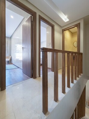 Ein modernes Interieur mit einer Holztreppe, einem sichtbaren Schlafzimmer mit Bett und einem Badezimmer mit Spiegel.