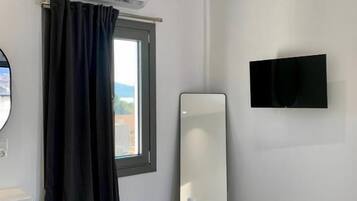 A hotel room with a bed, a flat-screen TV, a large mirror, and an air conditioning unit.
