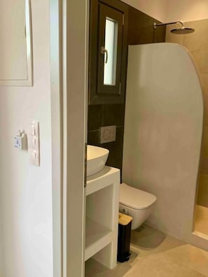 A bathroom with a toilet, a sink, and a shower enclosure. - Aitheria Suites Ios (Ios)