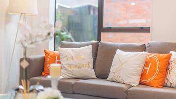 A living room with a sofa, decorative pillows, a lamp, and a vase with flowers.