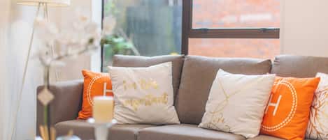 A living room with a sofa, decorative pillows, a lamp, and a vase with flowers.