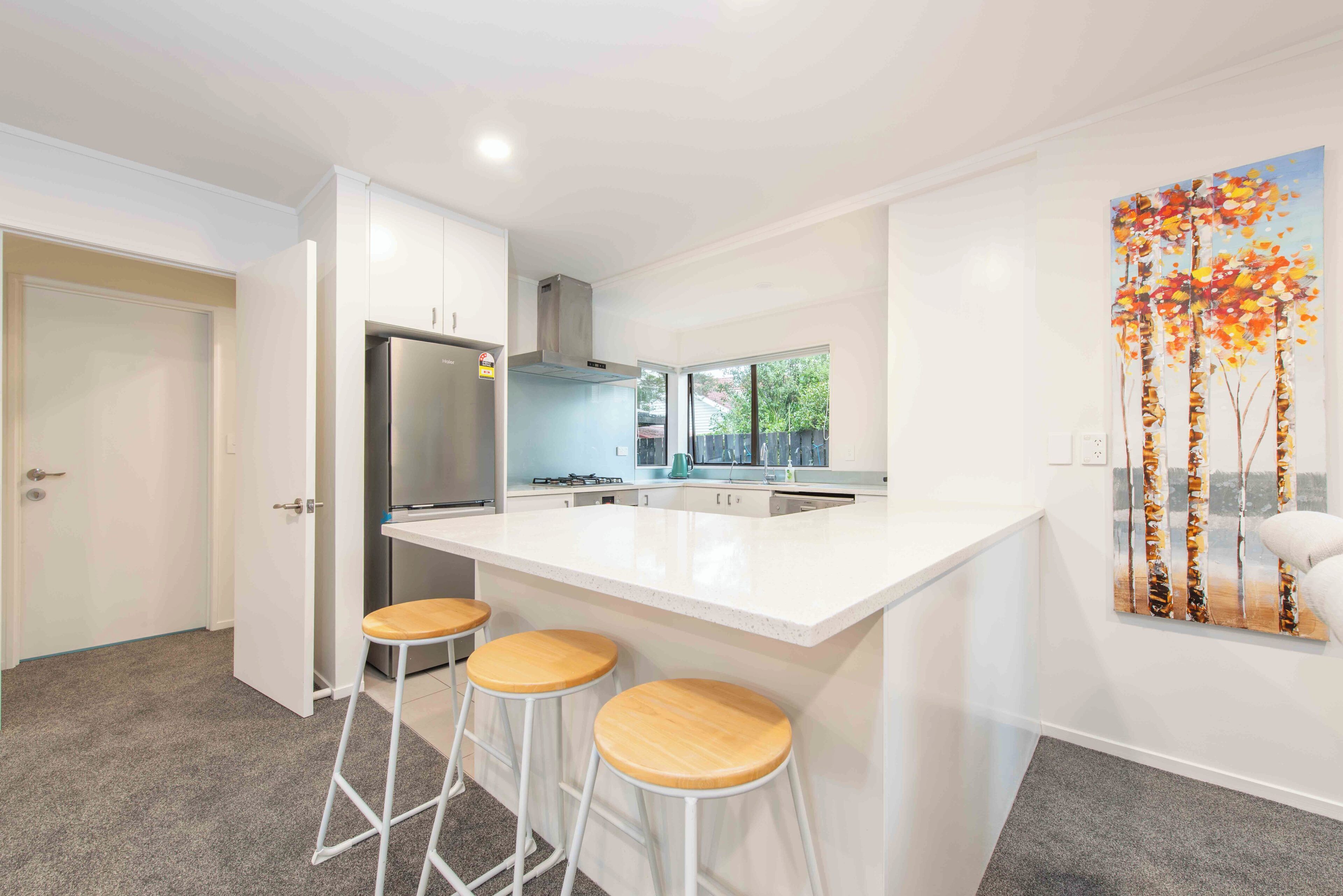 A modern kitchen with a central island, bar stools, and a painting on the wall.