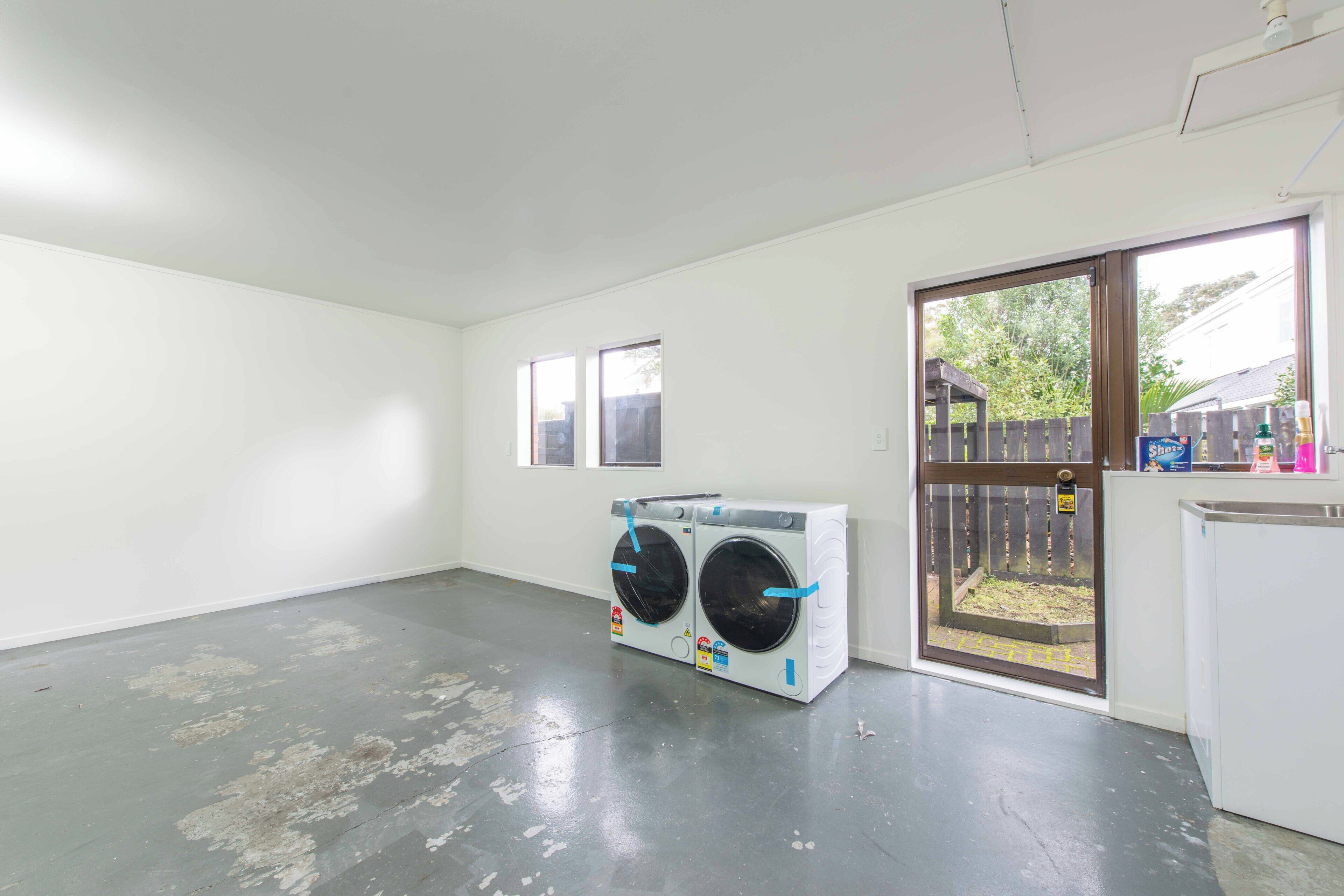 A laundry room with two stacked washing machines, a door leading outside, and a small window.