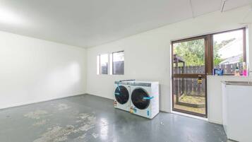 A laundry room with two stacked washing machines, a door leading outside, and a small window.