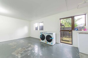 A laundry room with two stacked washing machines, a door leading outside, and a small window. - Cosy Greenlane Retreat | Calm & Unwind (Auckland)