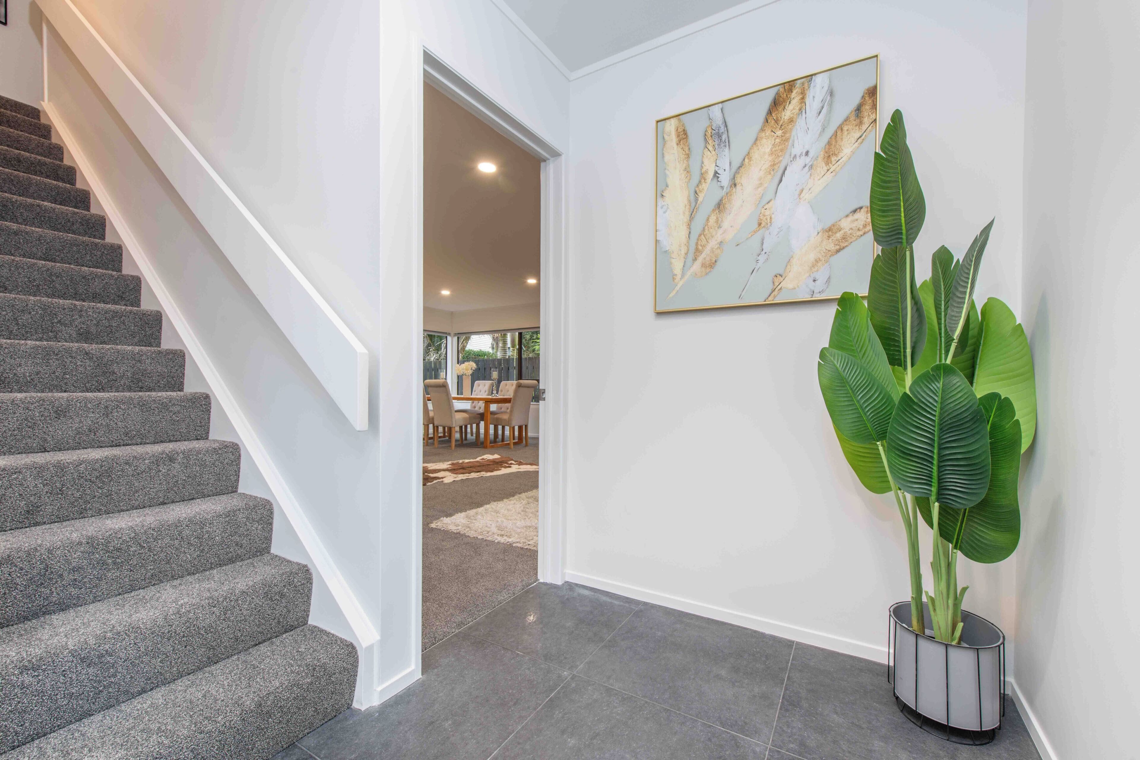 A staircase leading to a dining area with a large plant and a framed artwork on the wall.