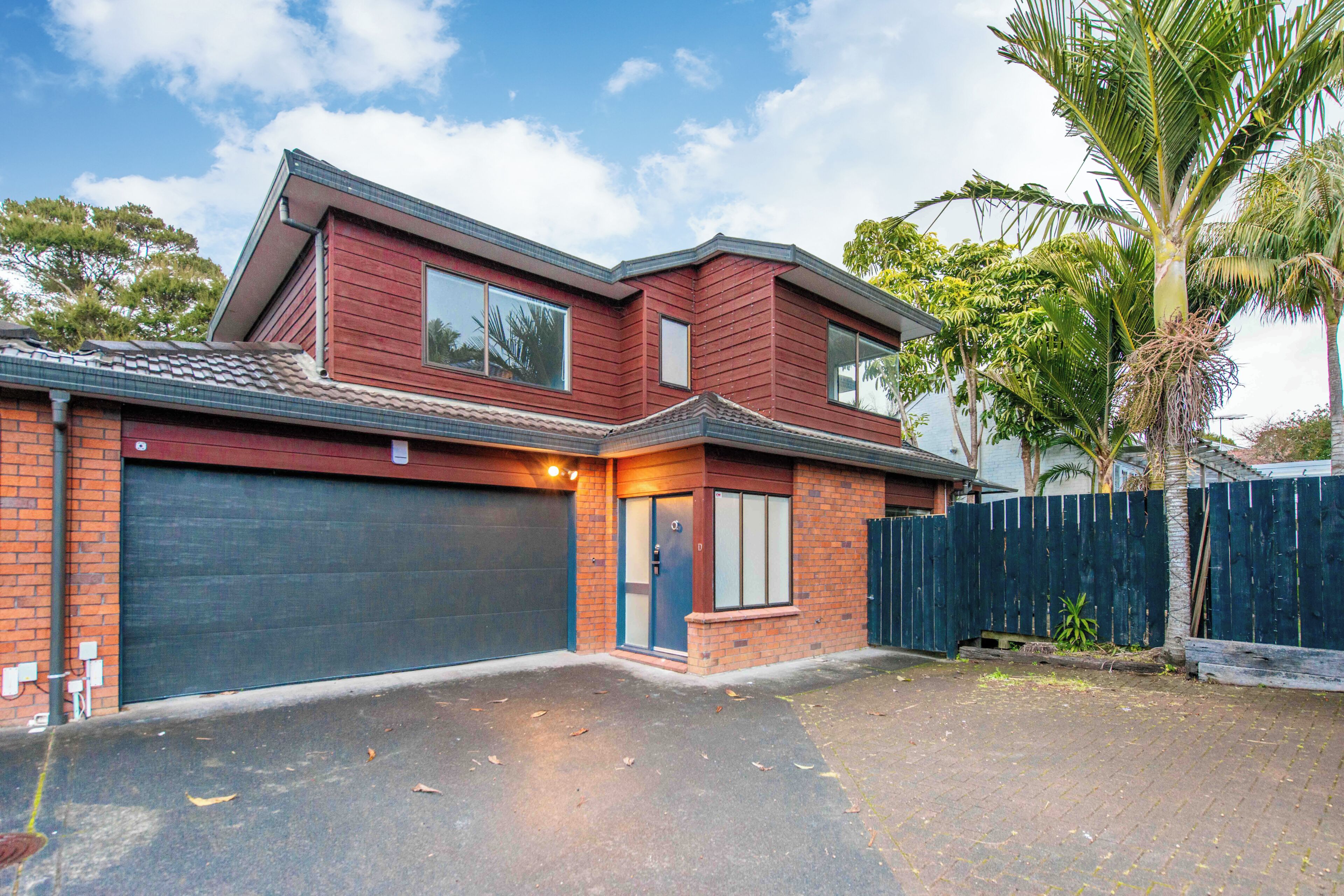 A two-story house with a garage, a fenced backyard, and a palm tree.
