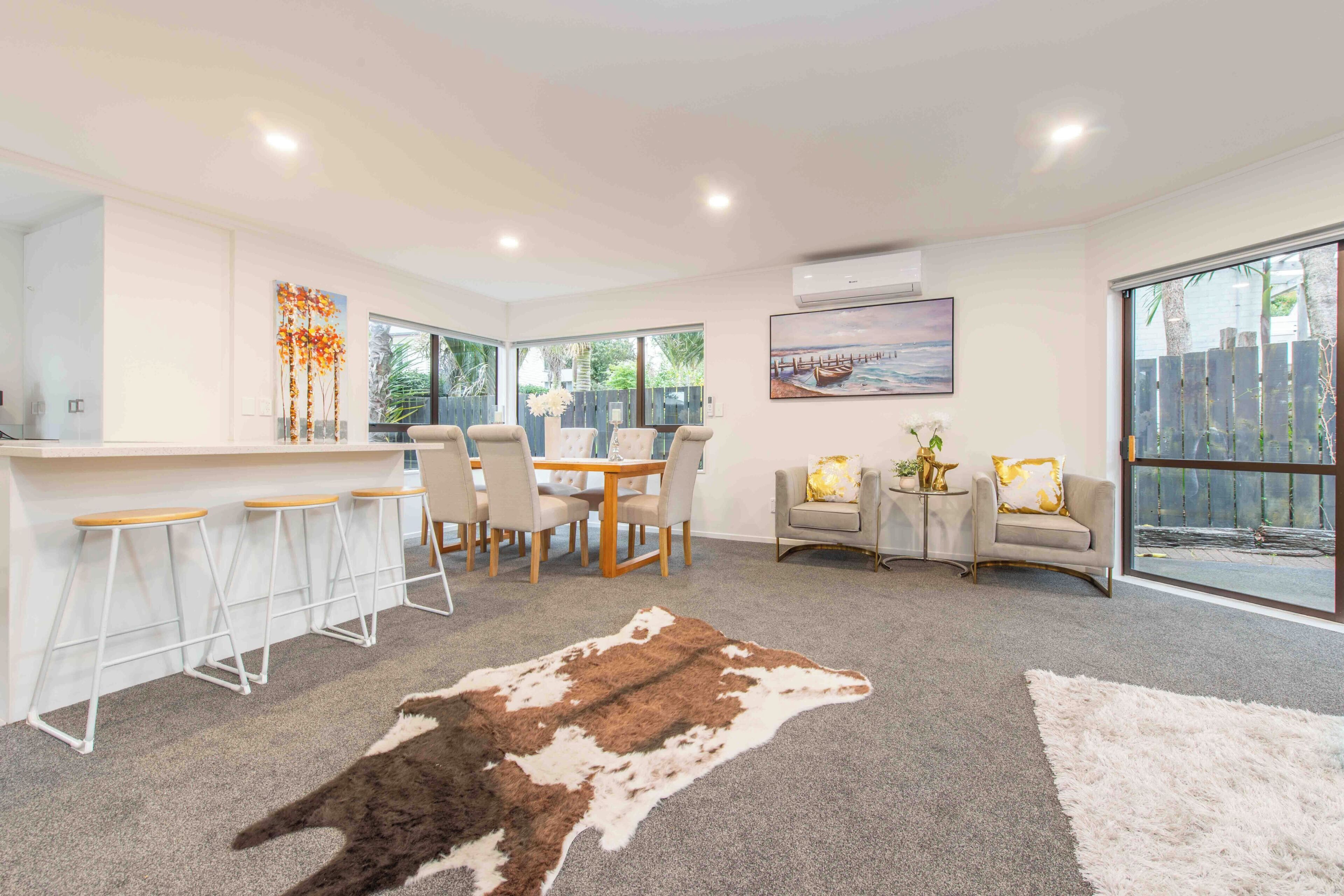 A modern living room with a dining area, large windows, and a view of the outdoors.