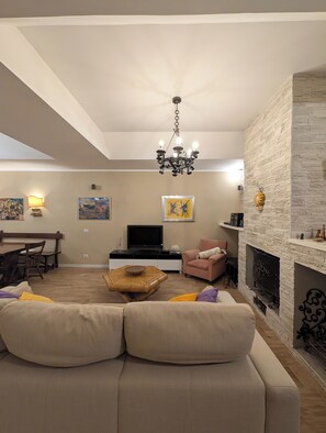 A living room with a sofa, a television, a fireplace, and a chandelier. - Casa Reds. Surrounded by nature, just a stone's throw from Rome (Formello)