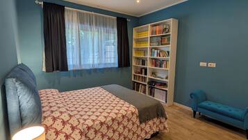 A bedroom with a bed, a bedside table with a lamp, a bookshelf, and a blue sofa.