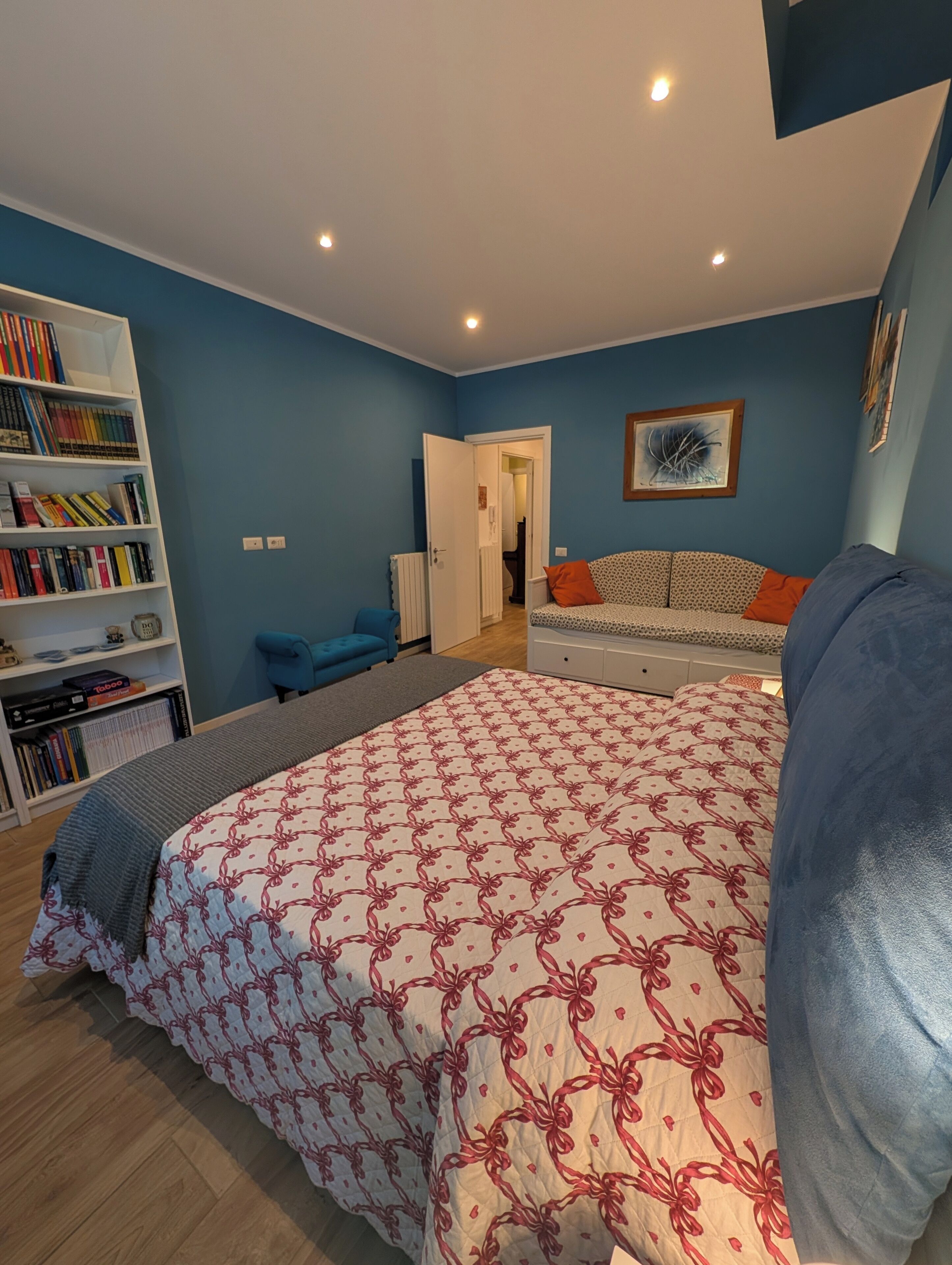 Ein Schlafzimmer mit Bett, Bücherregal, Sofa und einer Tür zu einem anderen Raum.
