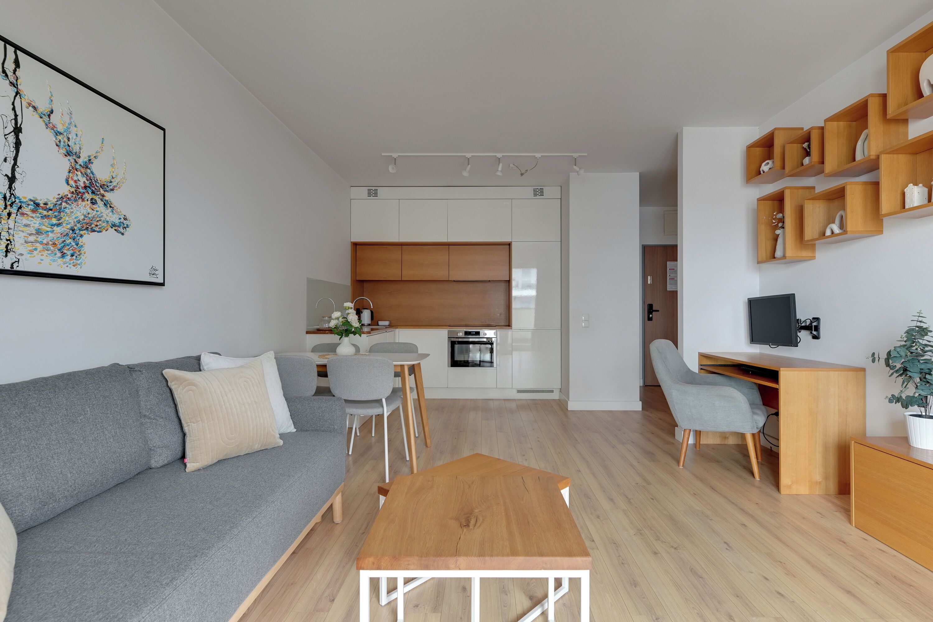 Ein modernes Wohnzimmer mit grauem Sofa, einem Holztisch und einem Essbereich mit weißem Tisch und Stühlen.